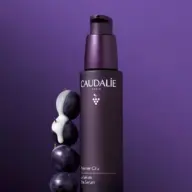 Caudalie Premier Cru Serum bottle with grapes and cream on purple background.