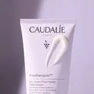 Caudalie Vinotherapist body cream tube with cream smear on a purple background.