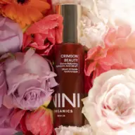 Crimson Beauty serum bottle surrounded by colourful flowers.