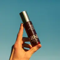 Hand holding NINI Organics bottle against clear blue sky.