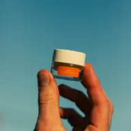 Hand holding a small jar with an orange label against a clear blue sky.