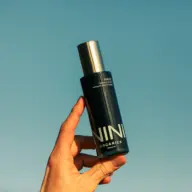 Hand holding NINI Organics bottle against a clear blue sky.
