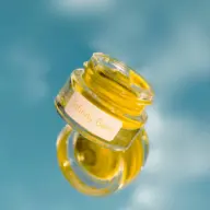 Glass jar of Infinity Balm with yellow contents against a blue background.