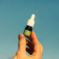 Hand holding a small dropper bottle against a clear blue sky.