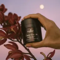 Hand holding Eco by Sonya Glory Cream near red flowers, moon in background.