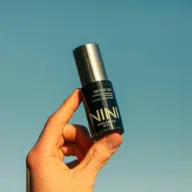 Hand holding NINI Organics Detox Oil bottle against clear blue sky.