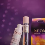 Neom Wellbeing bath foam and mist with packaging on a purple background.