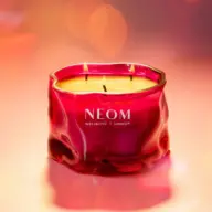 Red NEOM candle with three wicks on a pink background.