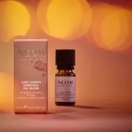 NEOM Cosy Nights Essential Oil Blend with packaging, 10ml bottle, warm bokeh background.