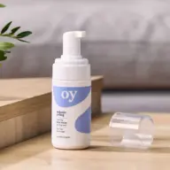 Organic Young foaming face wash on wooden surface, cap off, with plant in background.