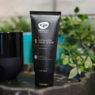 Black tube of Green People exfoliating face scrub for men, 90% organic, on a table with plants.