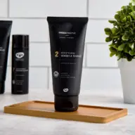 Black tube of Green People Soothing Wash & Shave on a wooden tray, plant in background.
