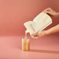 Hands pouring liquid from refill pouch into NEOM hand wash bottle.