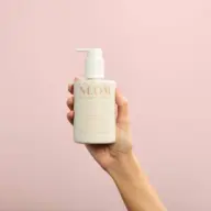 Hand holding NEOM lotion bottle against a pink background.