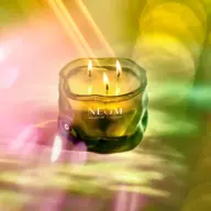 Green glass candle with three flames, labelled "NEOM Wellbeing London" against a colourful background.