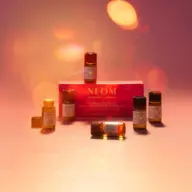 NEOM essential oil set with six small bottles on a pink surface, warm lighting.