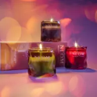 Three lit NEOM candles in green, brown, and red glass jars with a branded box behind.