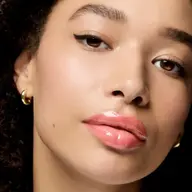 Close-up of a person with glossy pink lips, winged eyeliner, and gold hoop earrings.