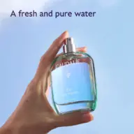 Hand holding Caudalie Eau des Vignes bottle against blue sky. Text: "A fresh and pure water".
