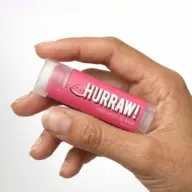 Hand holding Hurraw! watermelon lip balm tube.
