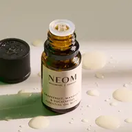 Open bottle of NEOM essential oil with drops on a surface.