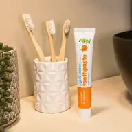 Tube of organic children's toothpaste beside bamboo toothbrushes in a holder.