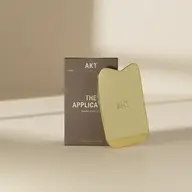 Gold AKT applicator with packaging on a beige surface.