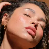 Person with glowing skin, eyes closed, wearing gold hoop earrings. Text: "Living Luminizer".
