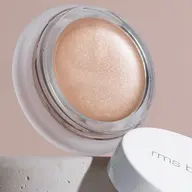 Open jar of shimmering peach cream with "rms beauty" on the white lid, set on a stone surface.