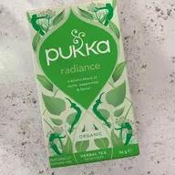 Pukka Radiance herbal tea box on a textured surface, featuring nettle, peppermint, and fennel.