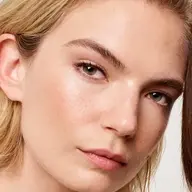 Close-up of a person with clear skin and light hair, looking towards the camera.
