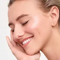 Woman with closed eyes smiling, touching her cheek.