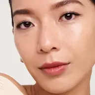 Close-up of a person with smooth skin and natural makeup, wearing a beige top.