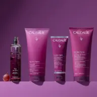 Caudalie Thé des Vignes products: fragrance, shower gel, hand cream, body lotion on purple background.