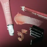 Lip balm tube, lip pencil, sharpener, and balm smear on a reflective surface.