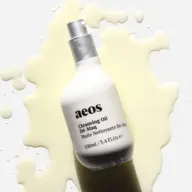 Aeos Cleansing Oil bottle on a light background with oil splatters.