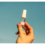 Hand holding a small spray bottle with a pink label against a clear blue sky.