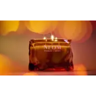 Amber glass candle with "NEOM Wellbeing London" text, lit with three flames.