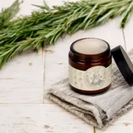 Brown jar of cream on grey cloth, rosemary sprigs in background.