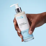 Hand holding The Organic Pharmacy Chamomile Cleansing Milk bottle.