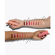Two arms showing lipstick swatches labelled Milla to Adriana, holding pink lipstick tubes.