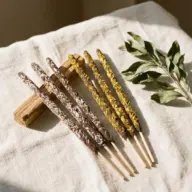 Incense sticks with herbs on linen cloth, wooden holder, and green leaves.