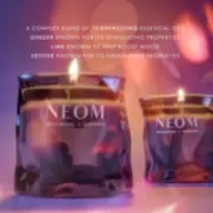 Two lit NEOM candles with text about energising essential oils in the background.