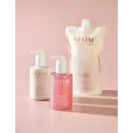 NEOM Complete Bliss hand wash, lotion, and refill pouch on a pink background.