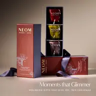 NEOM Wellbeing candle trio in red, yellow, and purple. Text: "Moments that Glimmer".