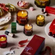 NEOM candles and products on a striped surface with decorative items and sweets.