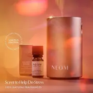 NEOM diffuser and Cosy Nights essential oil blend with packaging. Text: "Scent to Help De-Stress".