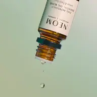 Amber bottle of NEOM essential oil with droplets falling.