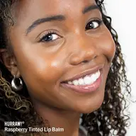 Smiling person wearing raspberry tinted lip balm. Text: "HURRAW! Raspberry Tinted Lip Balm".