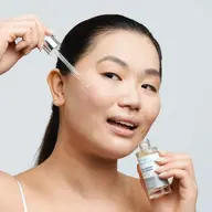 Person applying hyaluronic acid serum to cheek with dropper.
